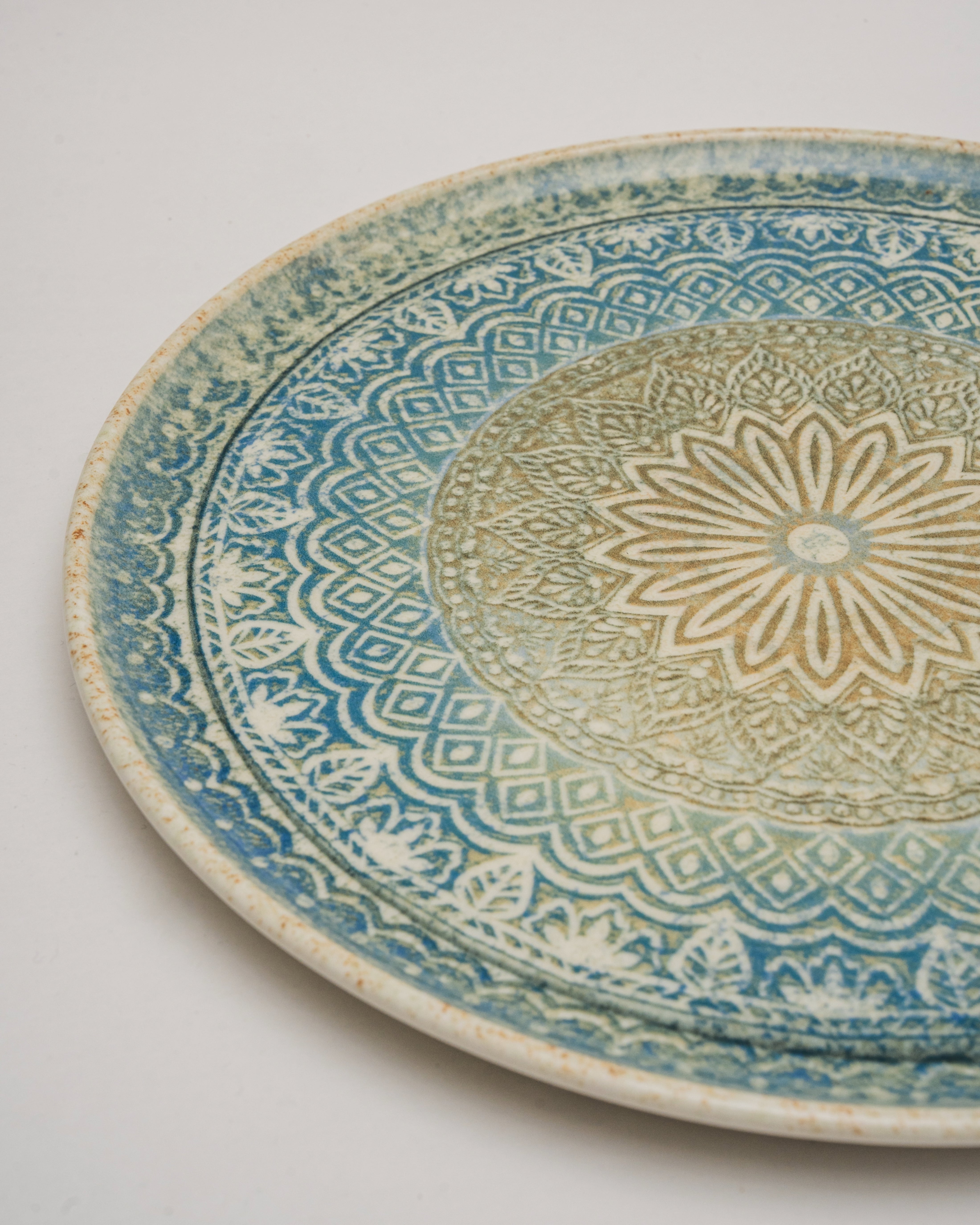 Angled view of Embroideries of Atlantis porcelain pizza plate showing pattern detail