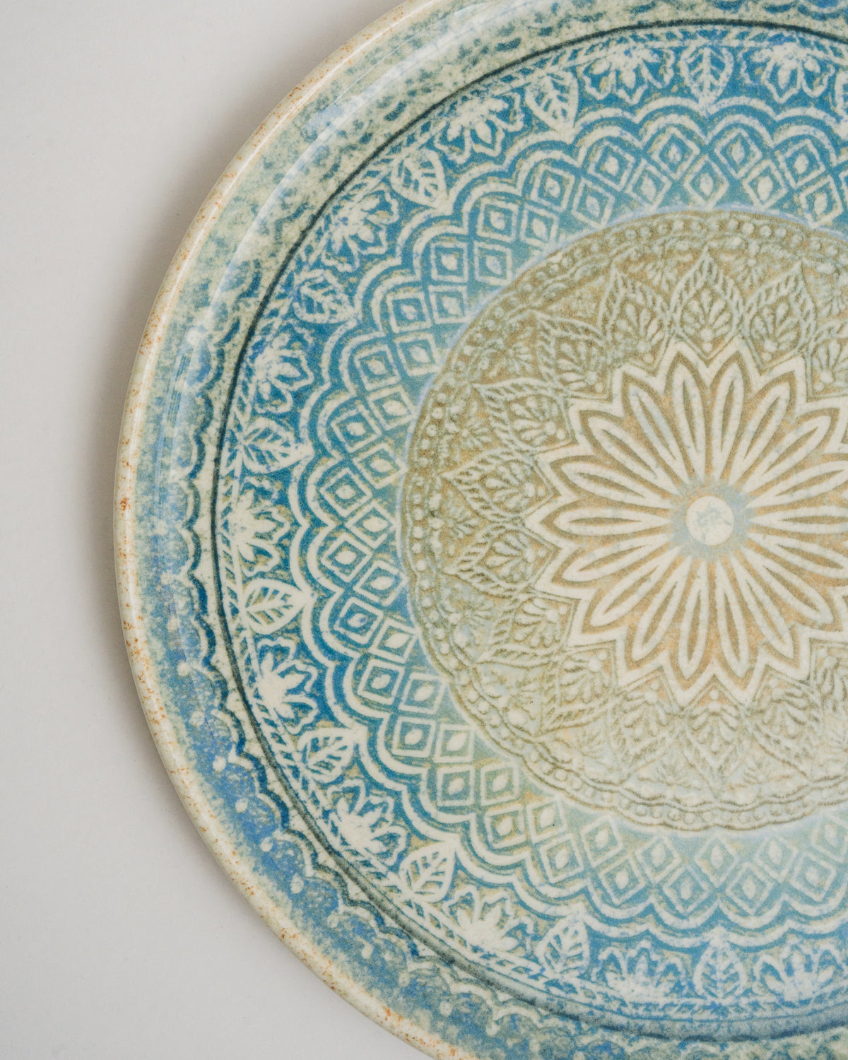Close overhead view of Embroideries of Atlantis porcelain pizza plate, blue and gold texture