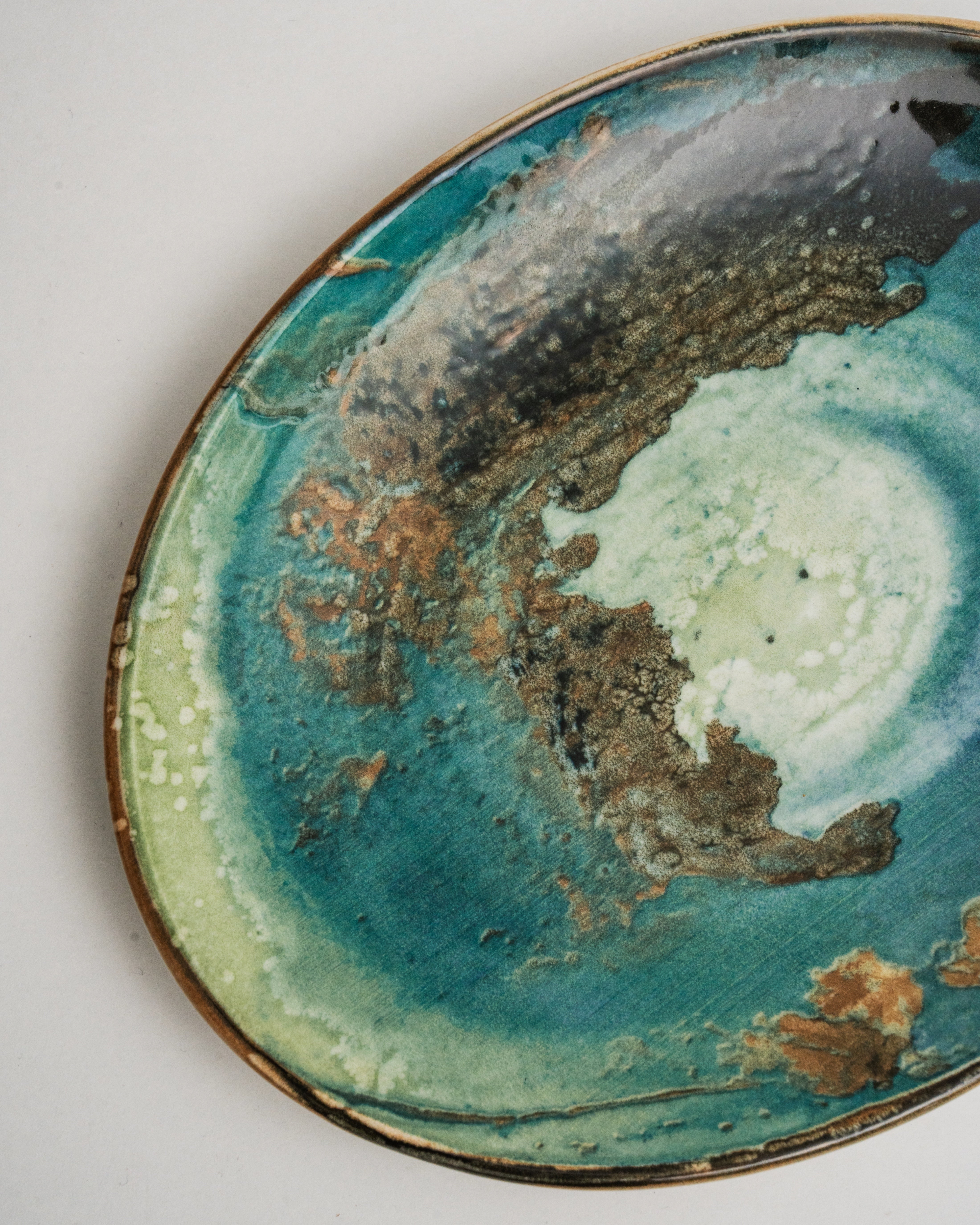 Angled view of Pelagos porcelain oval plate showing teal and gold glaze
