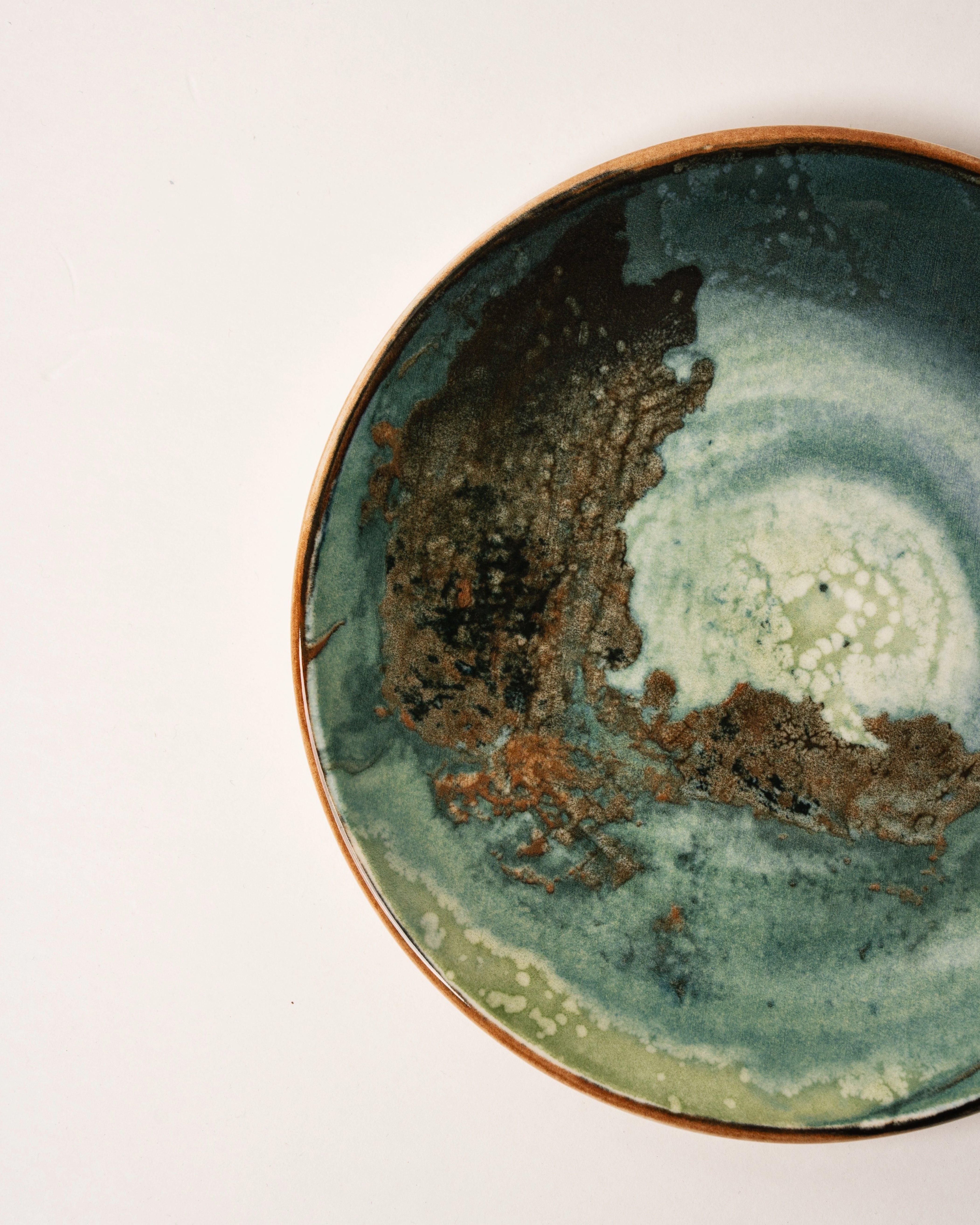 Angled view of Pelagos porcelain plate showing teal and gold glaze detail